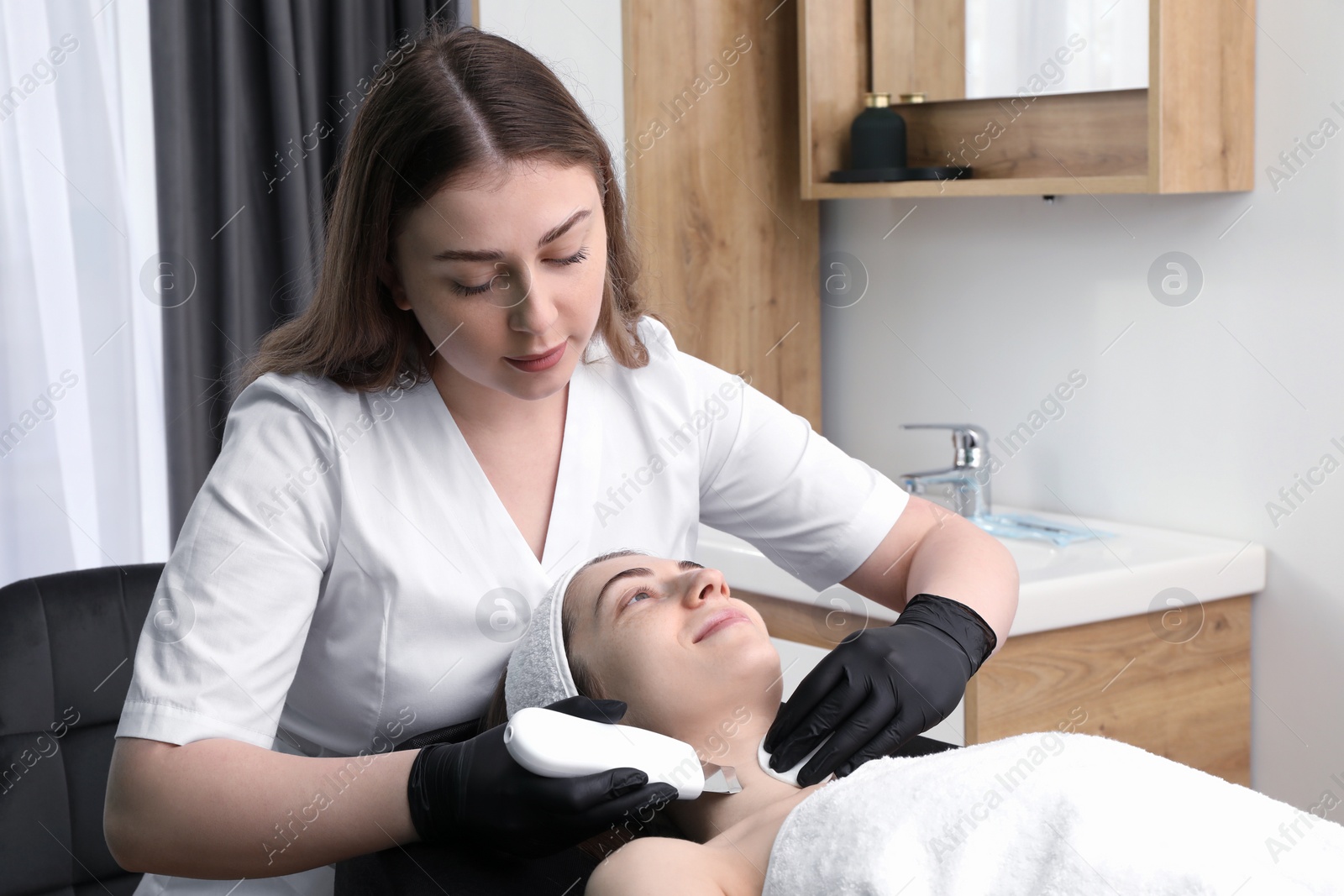 Photo of Cosmetologist using ultrasonic scrubber. Client having cleansing procedure in clinic