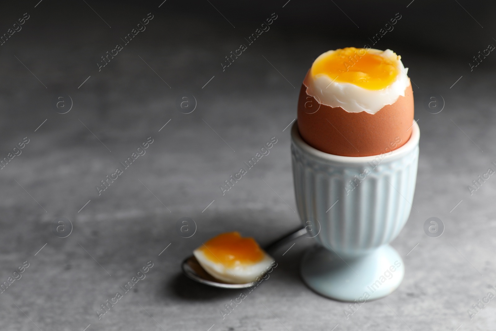 Photo of Fresh soft boiled egg in cup on grey table, closeup. Space for text