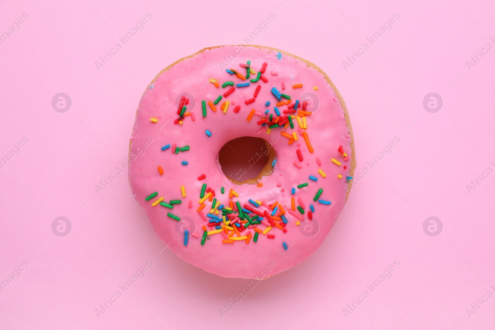 Photo of Tasty glazed donut decorated with sprinkles on pink background, top view