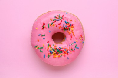 Tasty glazed donut decorated with sprinkles on pink background, top view