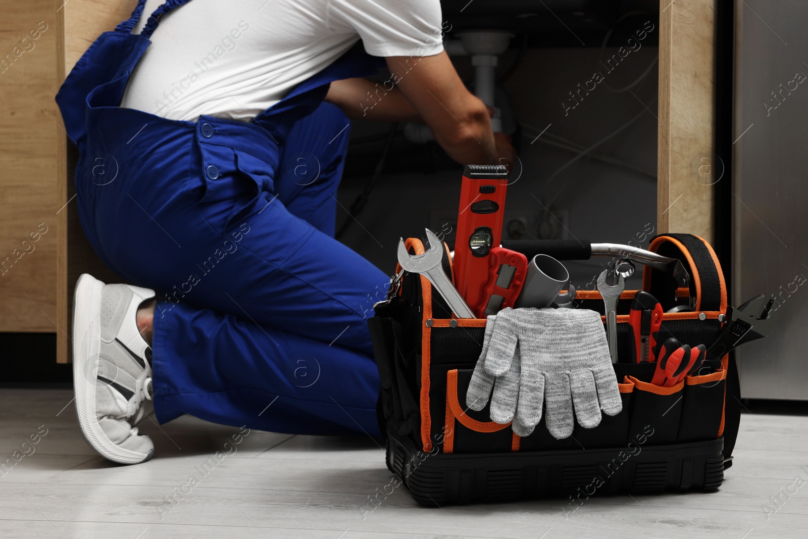 Photo of Professional plumber in uniform fixing sink indoors, closeup