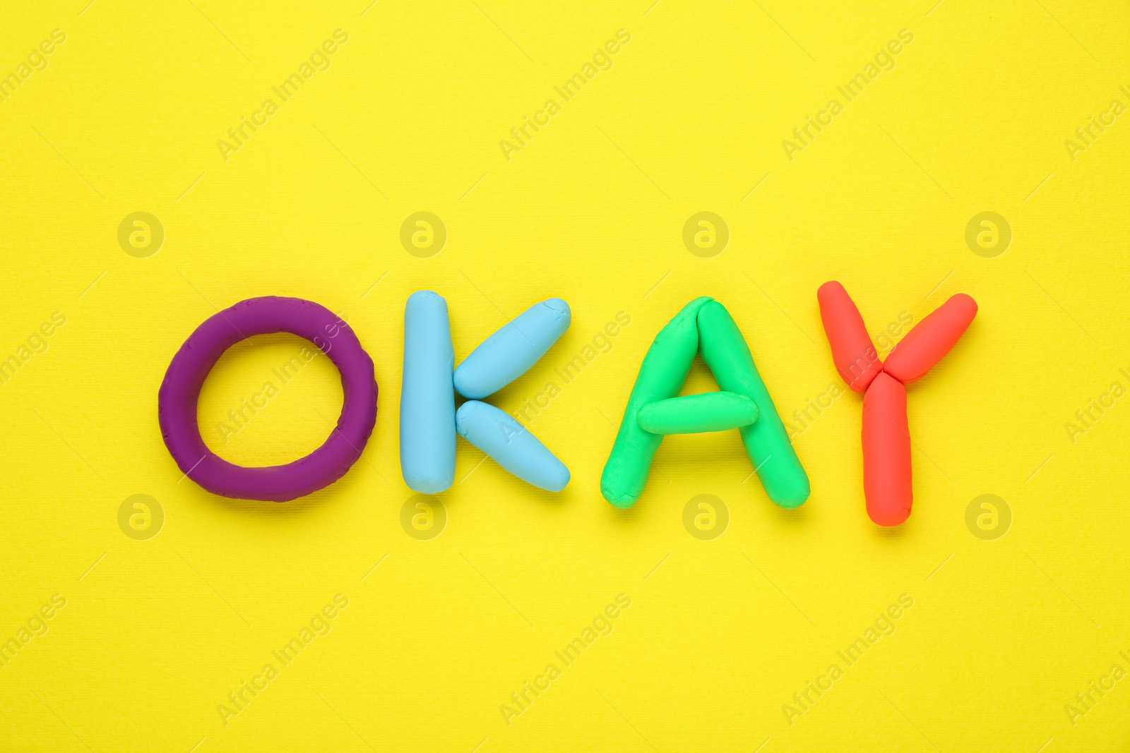 Photo of Word Okay made of colorful plasticine on yellow background, top view