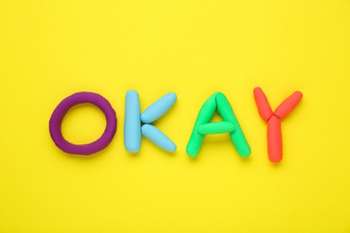 Photo of Word Okay made of colorful plasticine on yellow background, top view