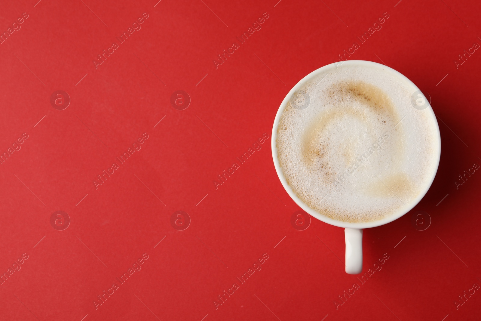 Photo of Tasty cappuccino in coffee cup on red background, top view. Space for text