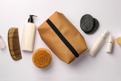 Compact toiletry bag, cosmetic products, comb and spa stones on white background, flat lay