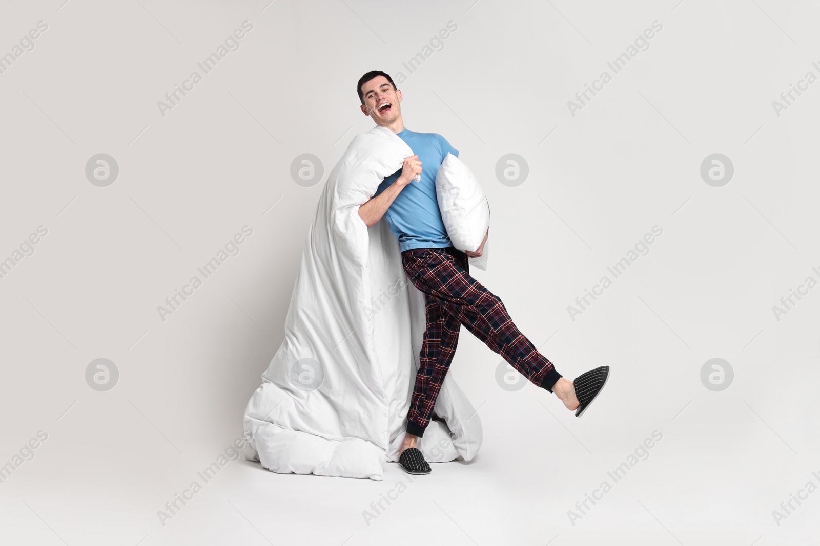 Photo of Happy man in pyjama with blanket and pillow on light grey background