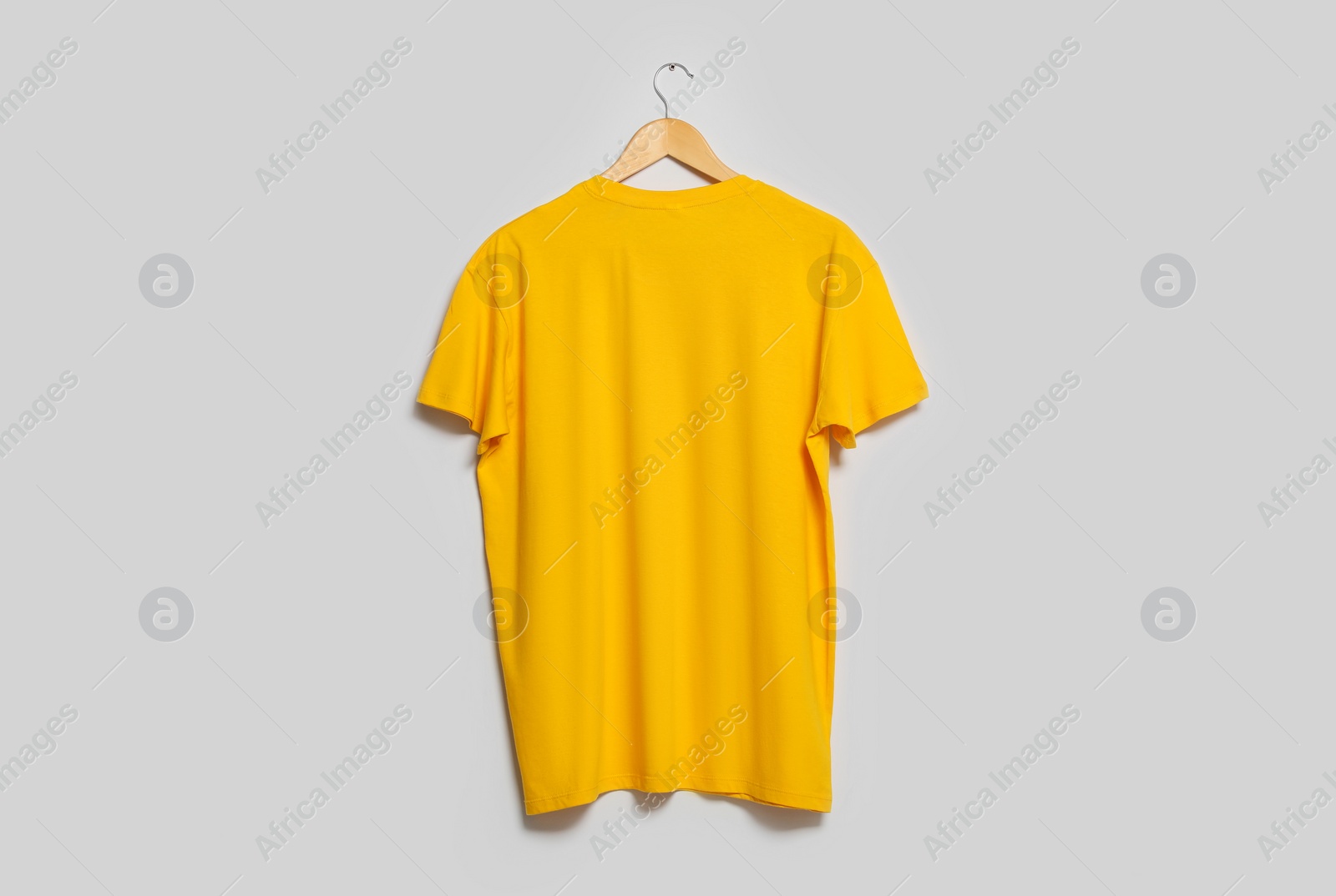 Photo of Hanger with yellow t-shirt on light wall. Mockup for design