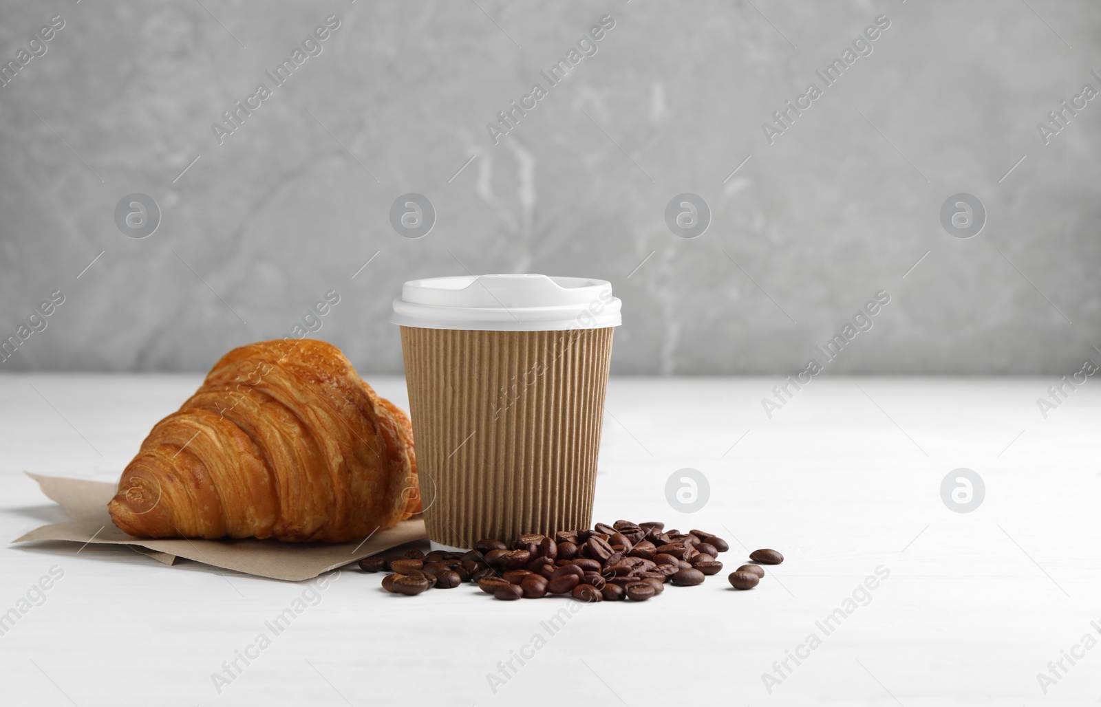 Photo of Coffee to go. Paper cup with tasty drink, croissant and beans on white wooden table. Space for text