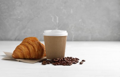 Photo of Coffee to go. Paper cup with tasty drink, croissant and beans on white wooden table. Space for text