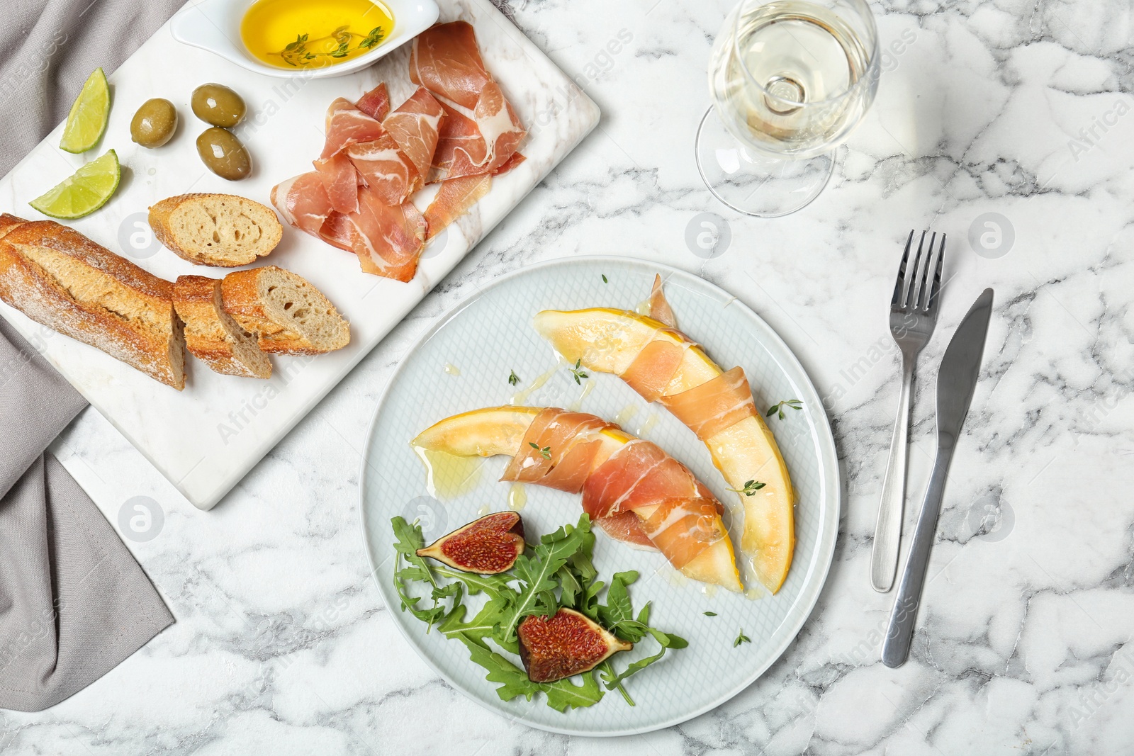 Photo of Flat lay composition with plate of melon slices and prosciutto on marble table