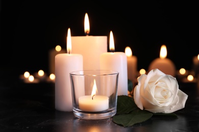 White rose and burning candles on table in darkness. Funeral symbol