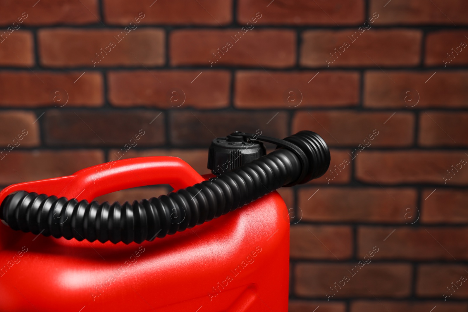 Photo of New red plastic canister against brick wall, closeup. Space for text