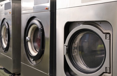 Photo of Row of modern washing machines in dry-cleaning, closeup