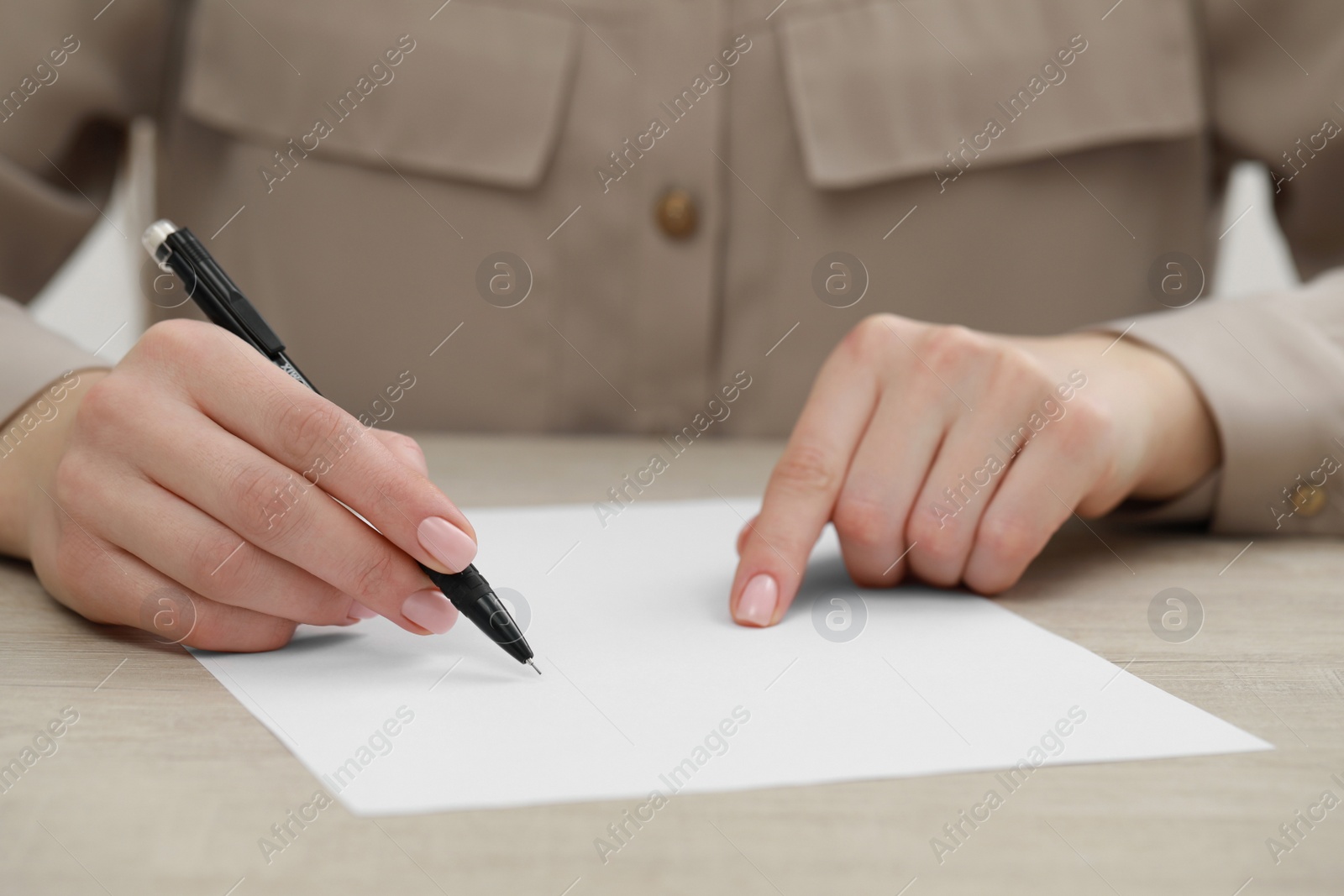 Photo of Woman writing on sheet of paper at light wooden table, closeup