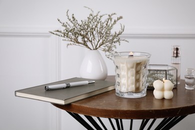 Photo of Burning soy candles, perfumes and stylish accessories on wooden table indoors