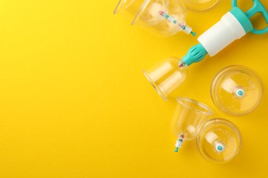 Photo of Plastic cups and hand pump on yellow background, flat lay with space for text. Cupping therapy