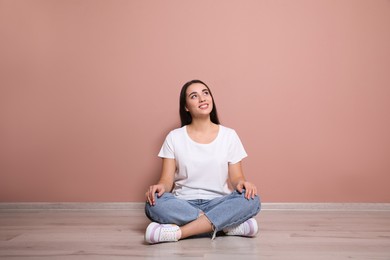Photo of Young woman sitting on floor near pink wall indoors