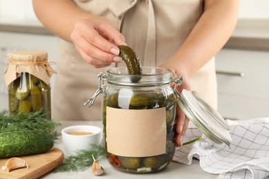 Woman taking pickled cucumber from jar at table in kitchen, closeup view. Space for text