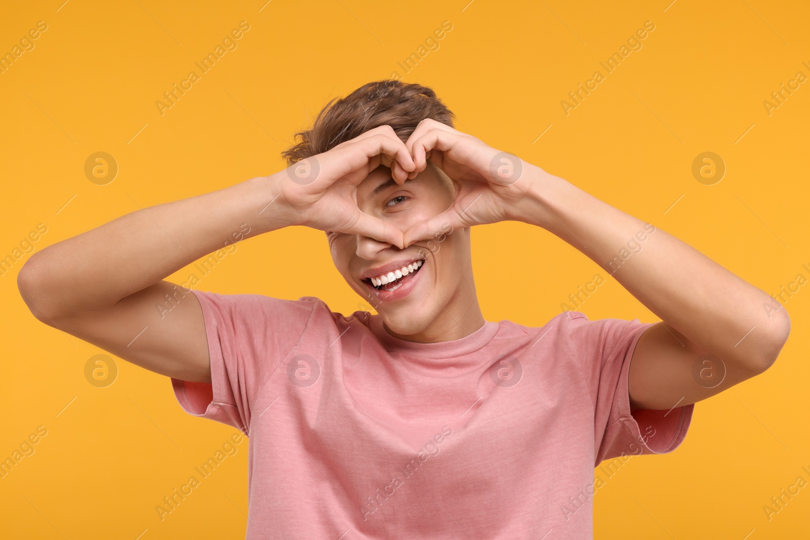 Photo of Happy man showing heart gesture with hands on orange background