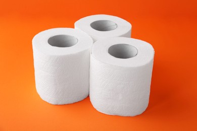 Photo of Soft toilet paper rolls on orange background, closeup