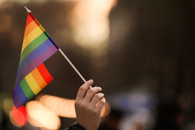 Woman holding small LGBT flag on city street, closeup. Space for text