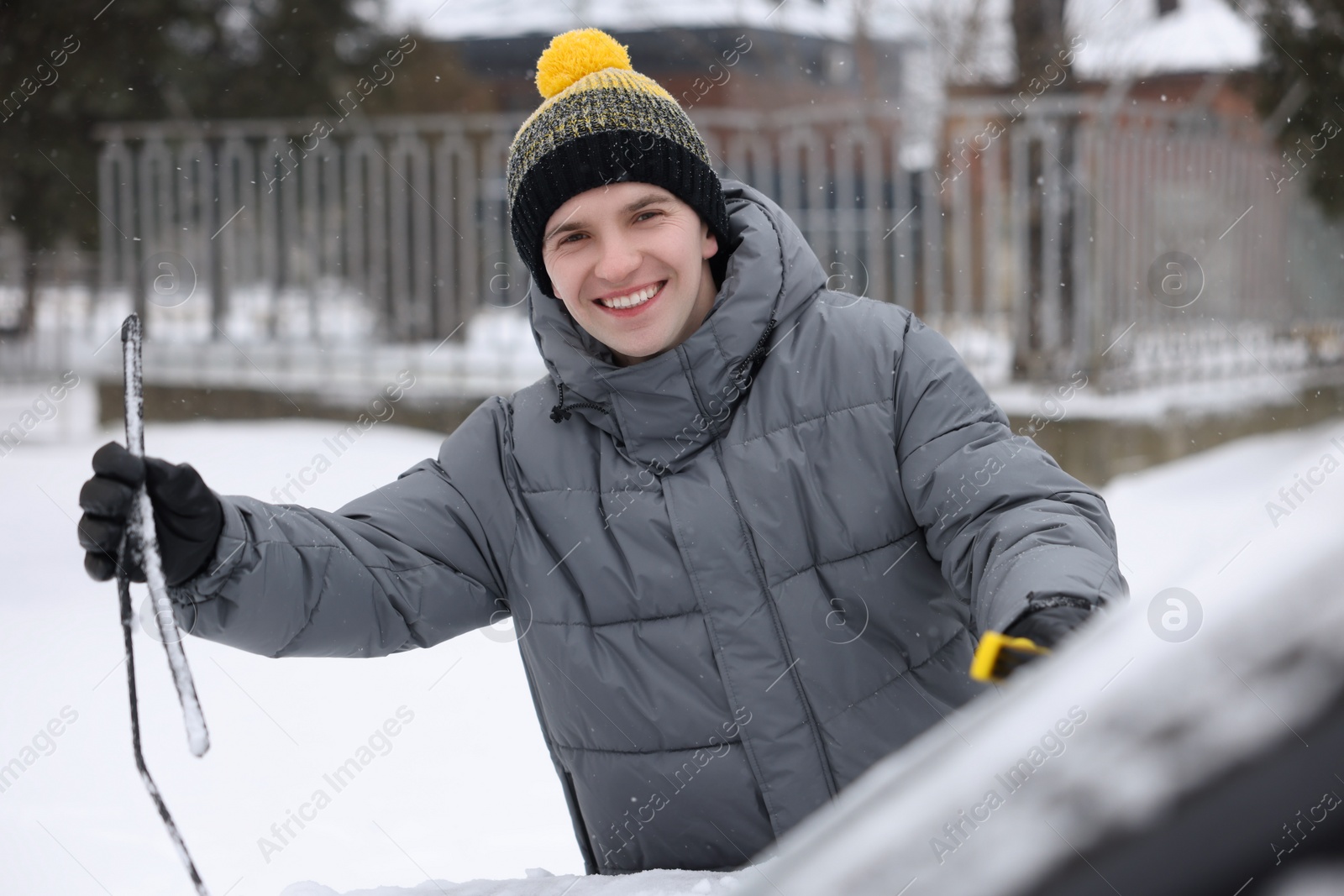 Photo of Man cleaning snow from car with brush outdoors