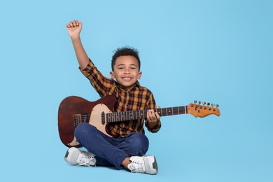 Cute African-American boy with electric guitar on turquoise background