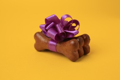 Photo of Bone shaped dog cookies with purple bow on yellow background, closeup