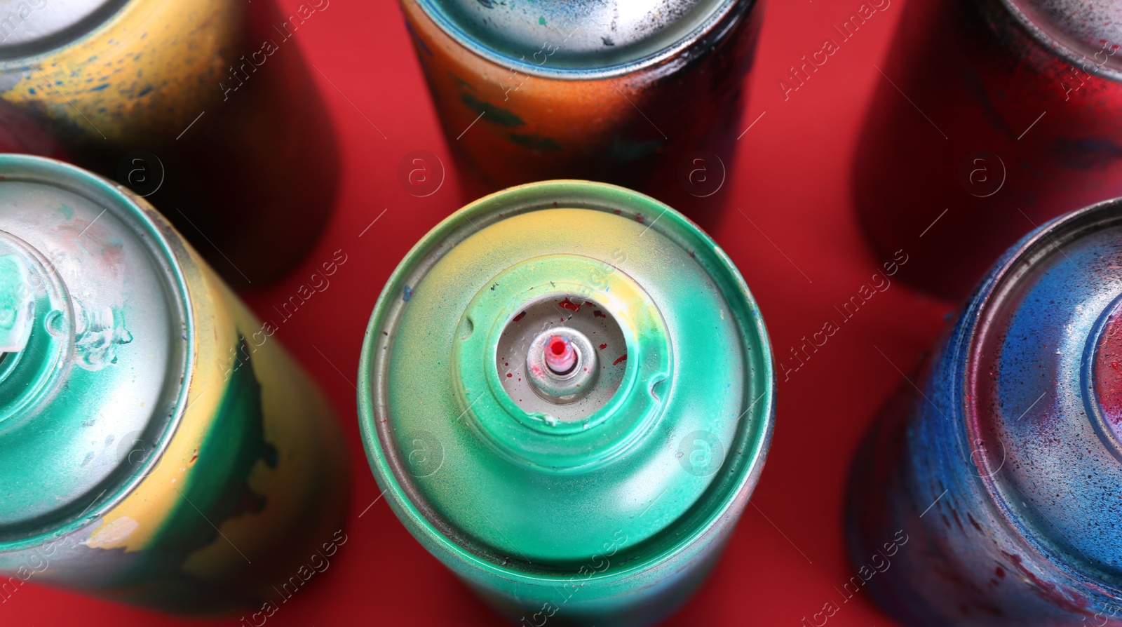 Photo of Many spray paint cans on red background, closeup