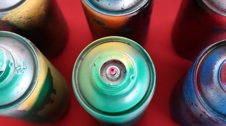 Many spray paint cans on red background, closeup