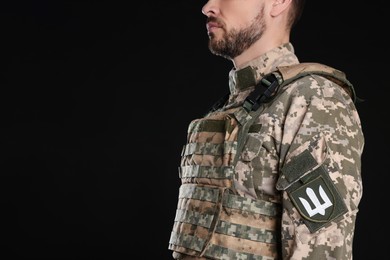 Photo of Soldier with Ukrainian trident on military uniform against black background, closeup. Space for text