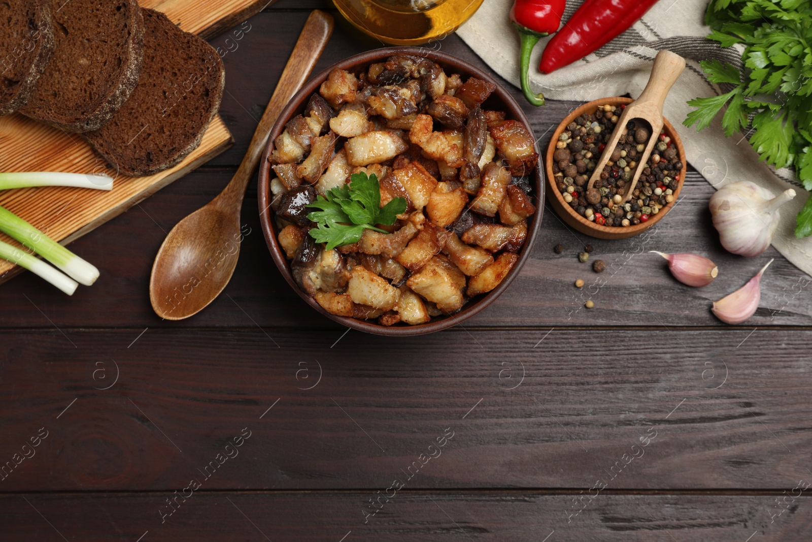 Photo of Tasty fried cracklings and different ingredients on wooden table, flat lay with space for text. Cooked pork lard