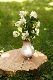 Photo of Bouquet of beautiful jasmine flowers in vase on wooden stump outdoors