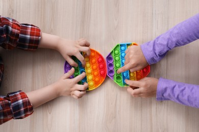 Photo of Little children playing with pop it fidget toys at wooden table, top view