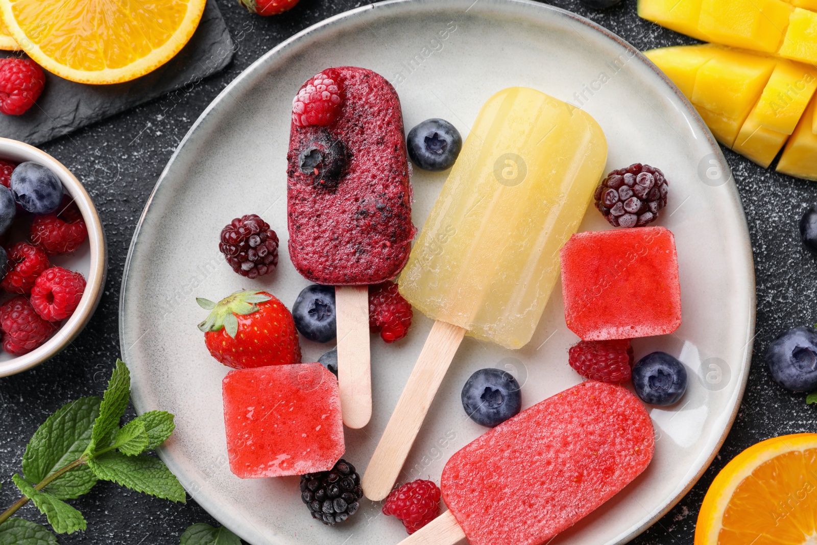 Photo of Plate of different tasty ice pops on black textured table, flat lay. Fruit popsicle