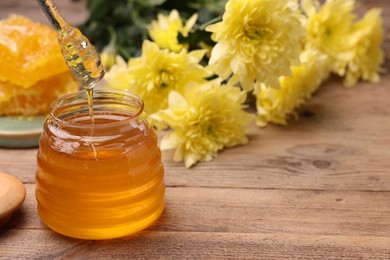 Photo of Pouring sweet golden honey from dipper into jar at wooden table, space for text