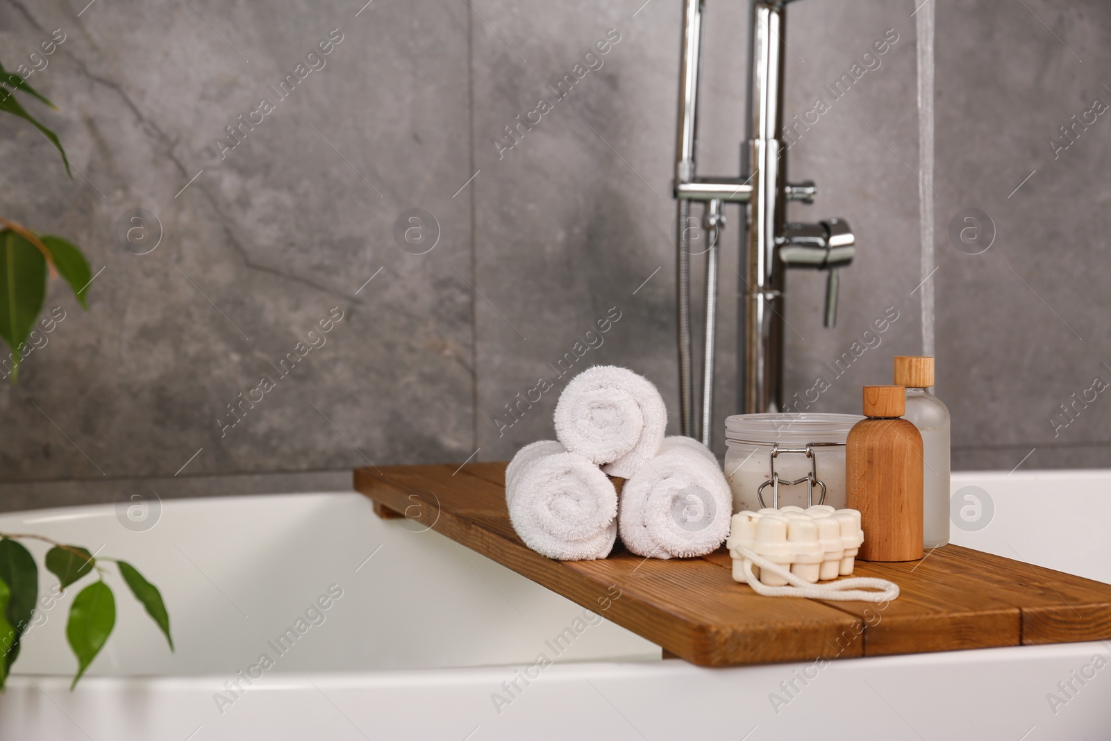 Photo of Wooden tray with spa products and towels on bath tub in bathroom. Space for text