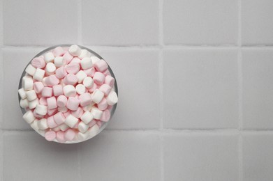 Bowl with delicious marshmallows on white tiled table, top view. Space for text