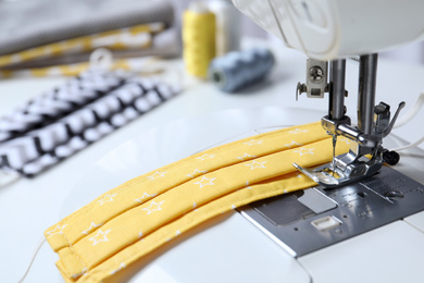 Photo of Sewing machine with homemade protective mask on table, closeup