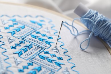 White fabric with blue Ukrainian national embroidery in hoop, needle and thread, closeup
