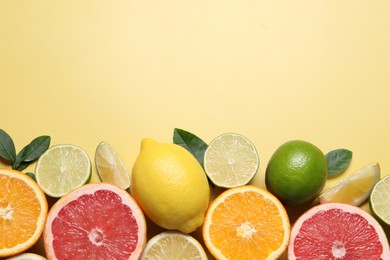 Photo of Different cut and whole citrus fruits on yellow table, flat lay. Space for text