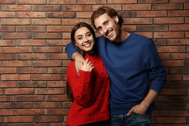 Young couple in warm sweaters near brick wall