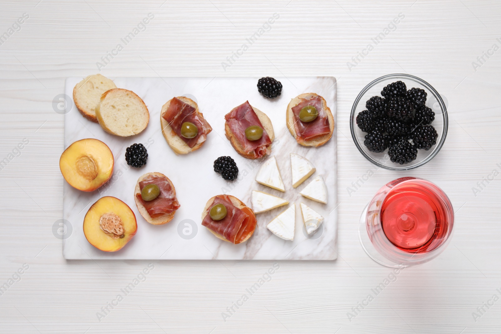 Photo of Glass of delicious rose wine and snacks on white wooden table, flat lay