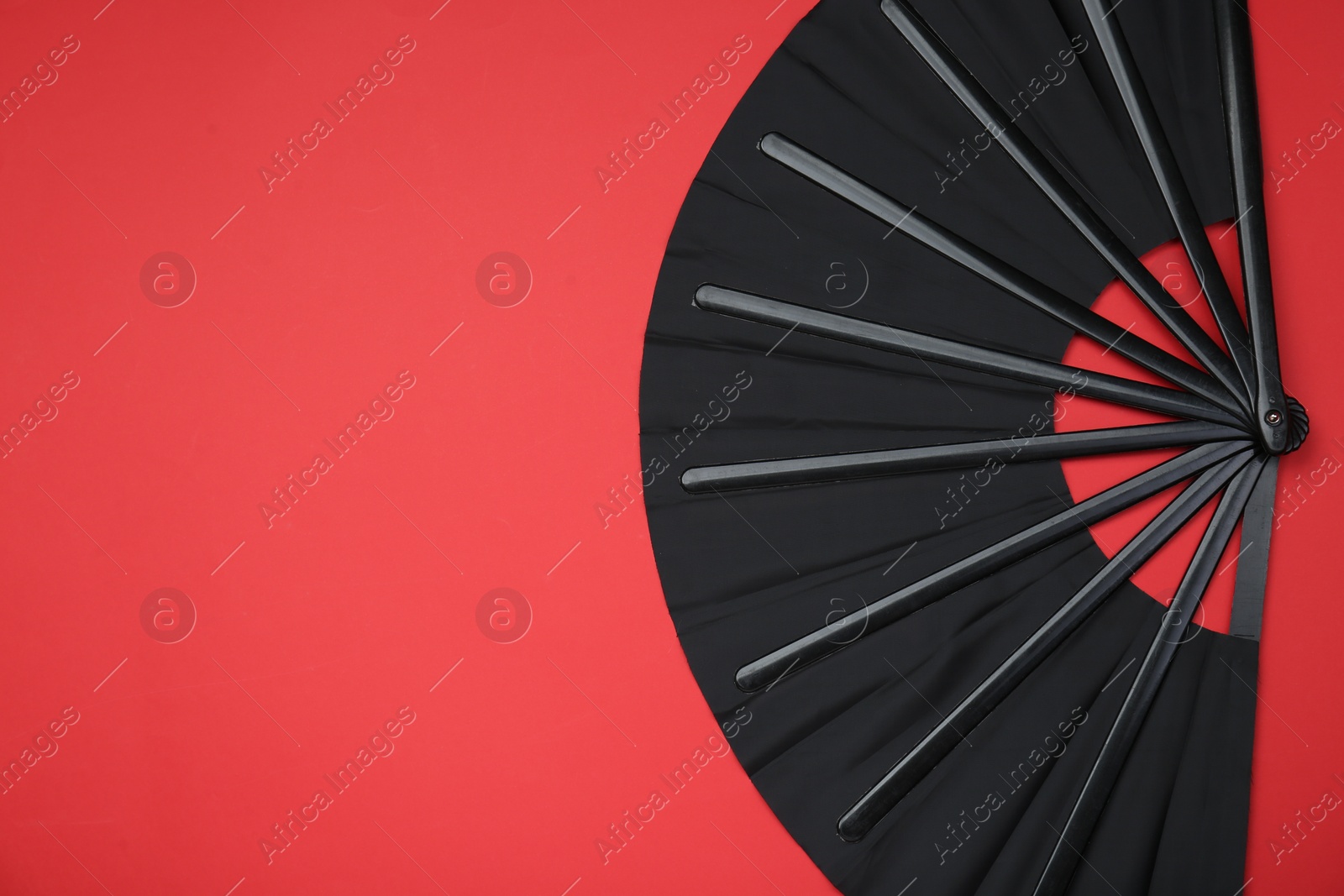 Photo of Stylish black hand fan on red background, top view. Space for text