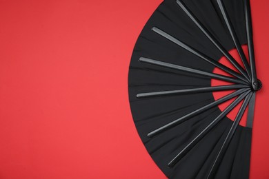 Photo of Stylish black hand fan on red background, top view. Space for text