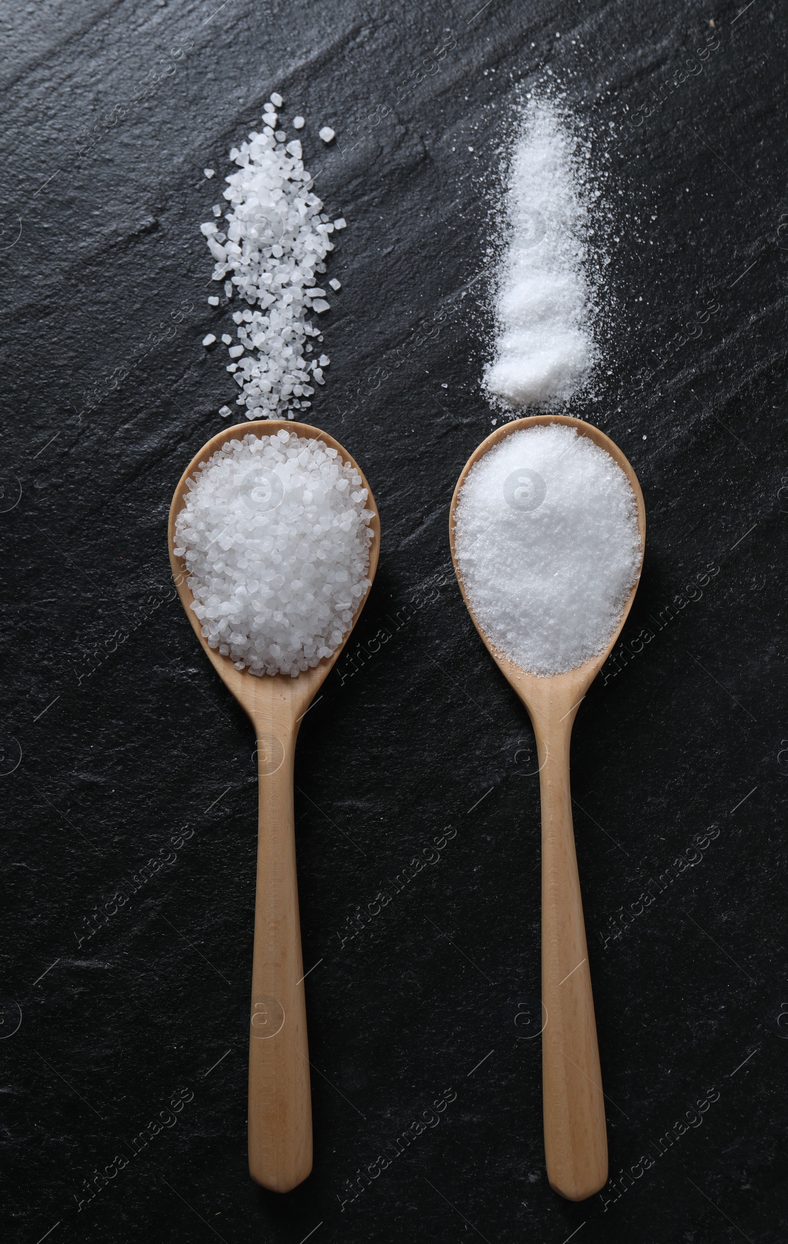 Photo of Organic salt in spoons on black table, flat lay