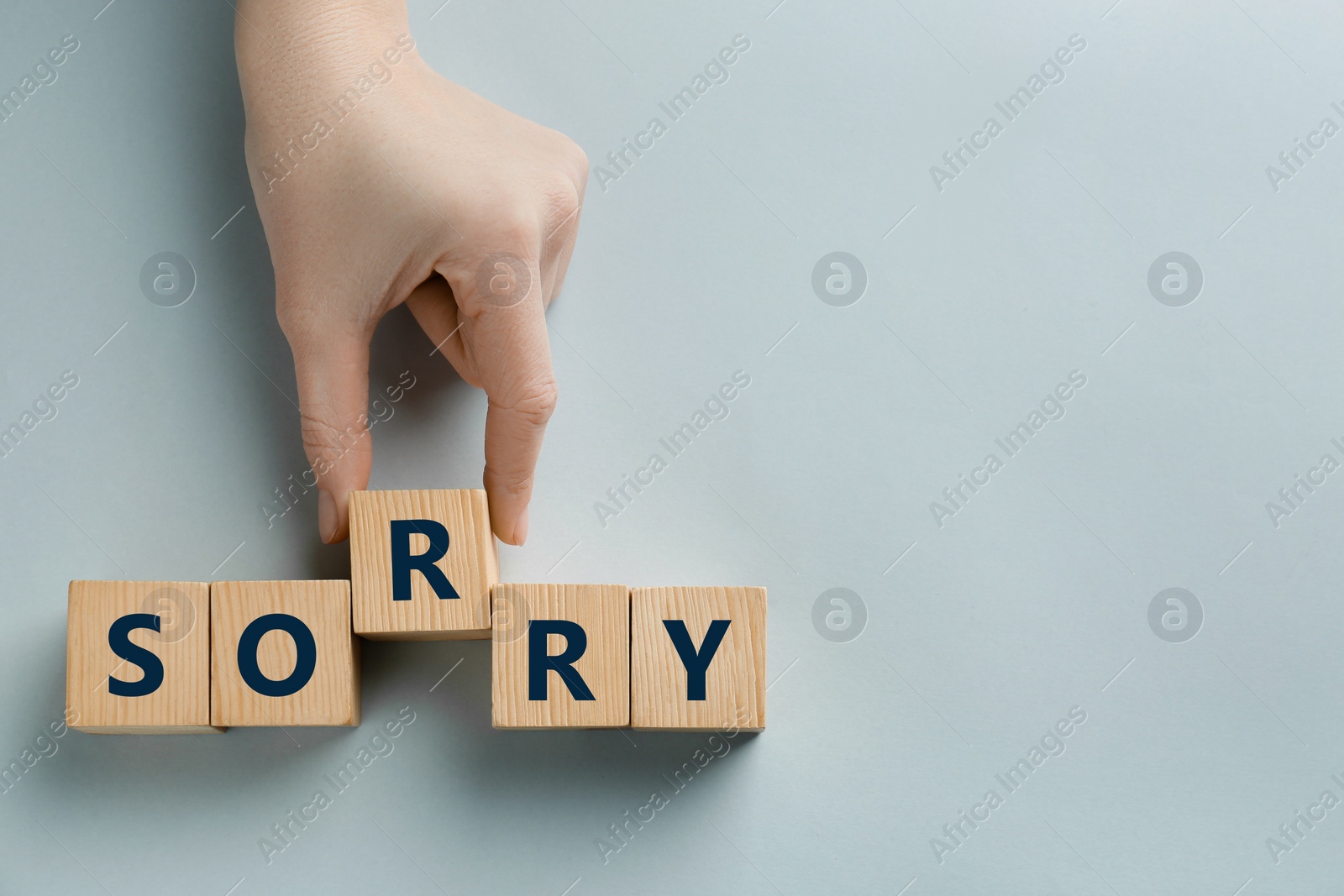 Image of Woman adding cube with letter R to make word Sorry on light background, top view. Space for text
