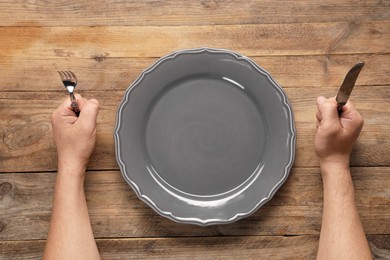 Photo of Man with cutlery and empty plate at wooden table, top view