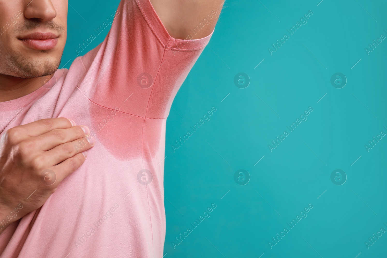 Photo of Young man with sweat stain on his clothes against light blue background, space for text. Using deodorant