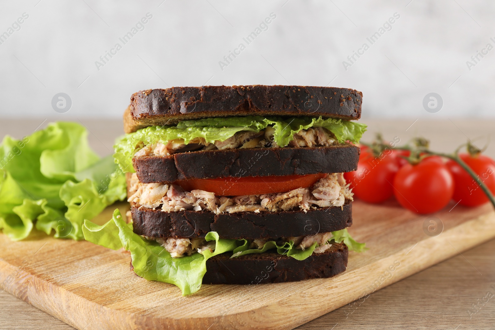 Photo of Delicious sandwich with tuna, tomatoes and lettuce on wooden table